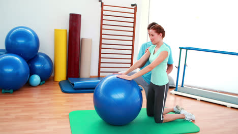 Trainer-helping-his-client-stretch-her-back-with-exercise-ball