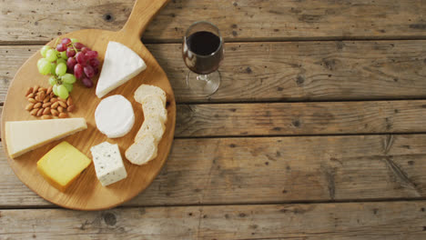 Video-of-cheeses,-bread,-grapes-and-nuts-on-board-and-red-wine-on-wooden-table,-with-copy-space