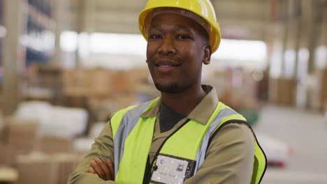 Portrait-of-african-american-male-worker-wearing-safety-suit-and-smiling-in-warehouse