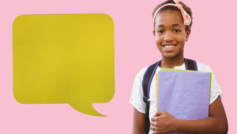 Animation-of-yellow-speech-bubble-over-smiling-african-american-schoolgirl-holding-book,-on-pink