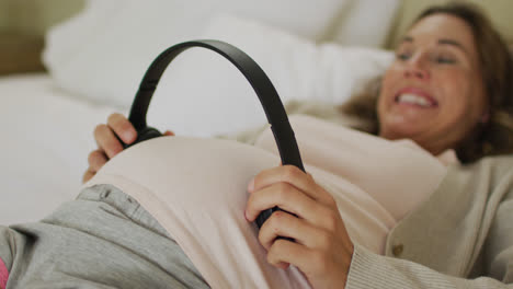 Midsection-of-happy-caucasian-pregnant-woman-holding-headphones-over-belly