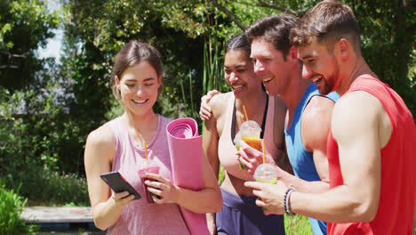 Happy-diverse-group-of-men-and-women-using-smartphone-and-talking-after-yoga-class-in-sunny-park