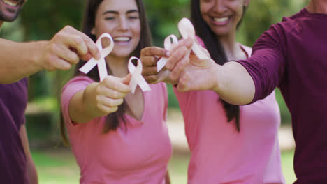 Portrait-of-diverse-group-of-men-and-women-smiling-and-holding-breast-cancer-ribbons-in-park