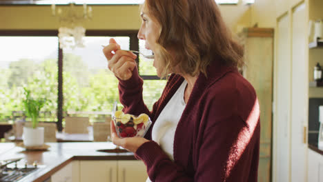 Profile-of-caucasian-pregnant-woman-standing-in-kitchen-and-eating-ice-cream