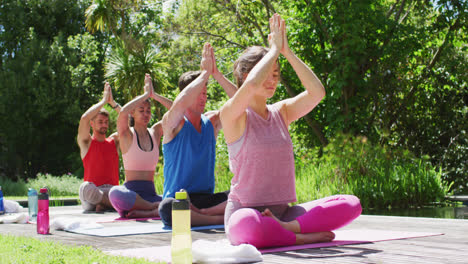 Grupo-Diverso-De-Hombres-Y-Mujeres-Practicando-Yoga-Sentados-En-Fila-Sobre-Colchonetas-En-Un-Parque-Soleado
