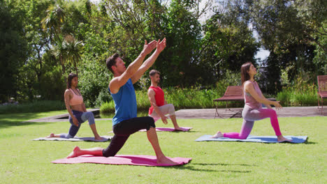 Grupo-Diverso-Practicando-Yoga-Con-Un-Instructor-Masculino,-Arrodillado-Sobre-Esteras-En-El-Parque-Soleado