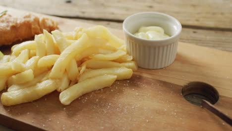 Video-of-fish-and-chips-with-lemon-wedge-and-dip-on-wooden-board,-on-rustic-table