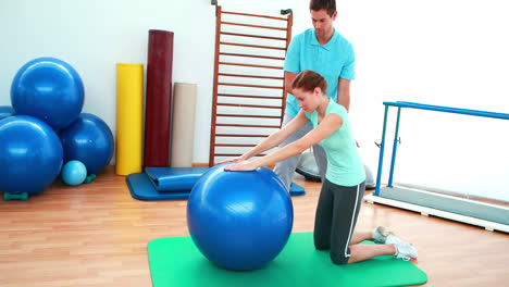 Trainer-helping-his-client-stretch-her-back-with-exercise-ball