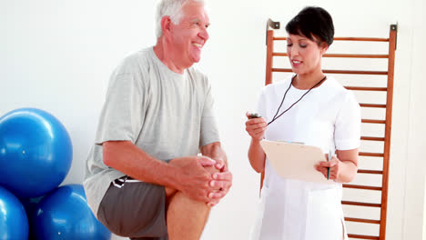 Smiling-physiotherapist-timing-elderly-patient-with-knee-bent