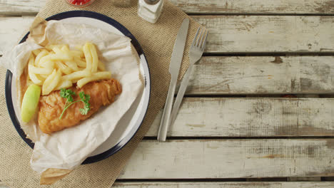 Video-of-fish-and-chips-on-plate,-salt-and-pepper-and-ketchup,-with-copy-space-on-wooden-table