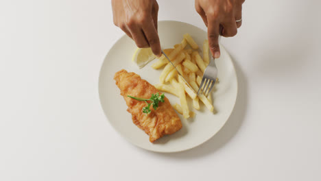 Video-overhead-shot-of-african-american-hands-eating-fish-and-chips-on-white-plate-with-copy-space