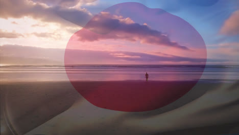 Digital-composition-of-waving-japan-flag-against-man-walking-on-the-beach