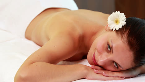 Peaceful-brunette-lying-on-massage-table-smiling-at-camera
