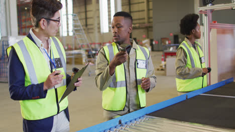 Diverse-male-and-female-workers-talking-next-to-conveyor-belt-in-warehouse