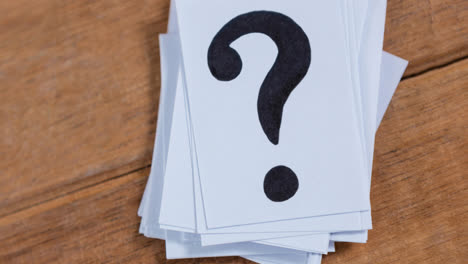 Stack-of-white-sheets-of-paper-with-question-mark-signs-on-wooden-table