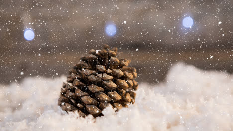 Snow-falling-over-pine-cone-on-snow-on-wooden-surface