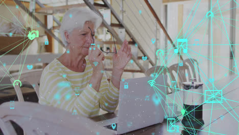 Animation-of-network-of-connections-with-icons-over-senior-caucasian-woman-using-laptop