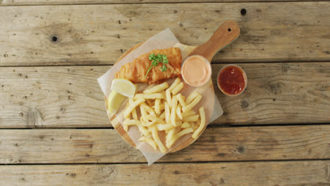 Video-of-fish-and-chips-on-wooden-board-with-dips,-with-copy-space-on-wooden-table