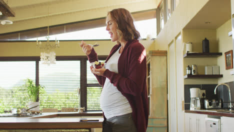 Mujer-Embarazada-Caucásica-Parada-En-La-Cocina-Y-Comiendo-Helado