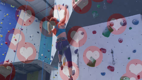 Multiple-heart-icons-floating-against-caucasian-fit-woman-wall-climbing-at-the-gym