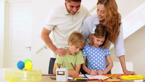 Glückliche-Eltern-Und-Kinder,-Die-Gemeinsam-Am-Tisch-Zeichnen-Und-In-Die-Kamera-Schauen