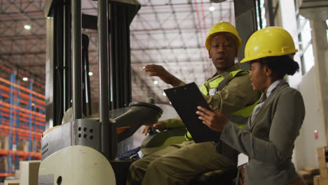 African-american-male-and-female-workers-wearing-safety-suits-and-talking-in-warehouse