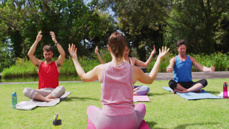 Rear-view-of-caucasian-female-instructor-practicing-yoga-with-diverse-group-in-park