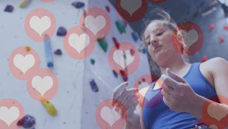 Multiple-heart-icons-floating-against-caucasian-fit-woman-applying-chalk-to-her-hands-at-the-gym