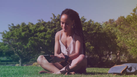 Spots-of-light-against-african-american-woman-using-smartphone-sitting-on-the-grass