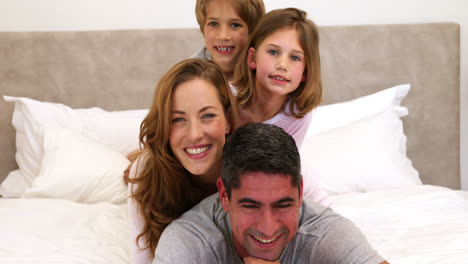 Süße-Eltern-Und-Kinder-Liegen-Auf-Dem-Bett-Und-Lächeln-In-Die-Kamera