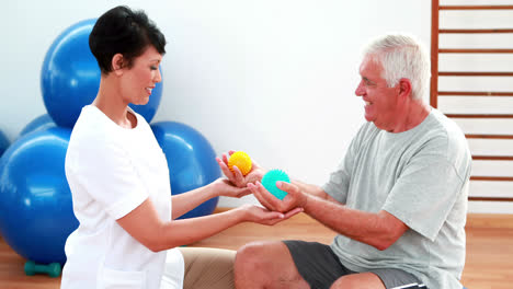 Fisioterapeuta-Sonriente-Apretando-Bolas-De-Masaje-Con-Paciente