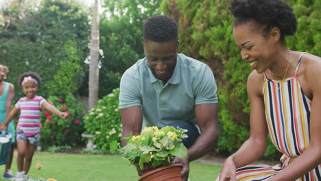 Happy-african-american-family-holding-watering-can-and-working-in-garden
