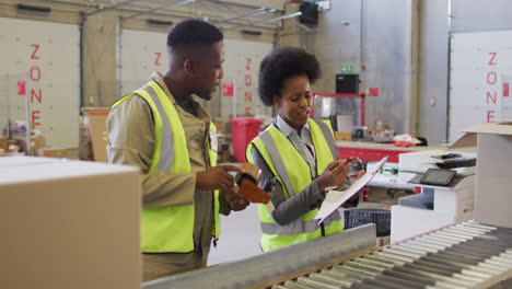 African-american-male-and-female-workers-with-clipboard-next-to-conveyor-belt-in-warehouse