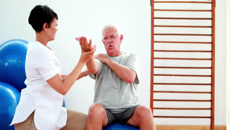 Smiling-physiotherapist-helping-elderly-patient-stretch-arm