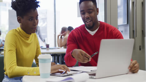 African-american-male-and-female-business-colleagues-talking-and-using-laptop-in-office