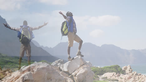 Composite-of-happy-african-american-man-hiking,-and-raising-arms-on-mountainside