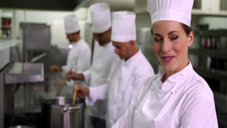 Head-chef-smiling-at-camera-with-team-behind-her