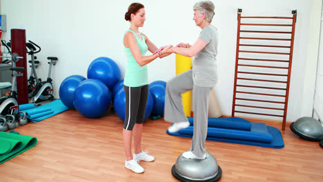 Trainer-helping-elderly-client-to-use-bosu-ball