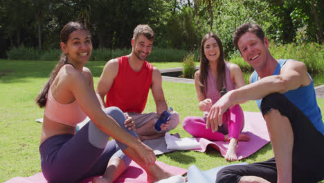 Portrait-of-smiling-male-yoga-instructor-and-happy-diverse-group-sitting-on-mats-in-sunny-park