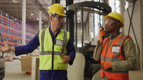 Diverse-male-workers-wearing-safety-suits-and-talking-in-warehouse