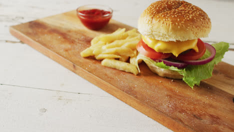 Video-of-cheeseburger,-chips-and-bowl-of-ketchup-on-wooden-board