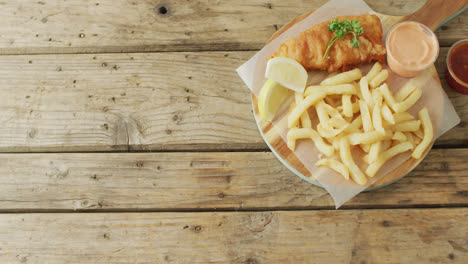 Video-of-fish-and-chips-on-wooden-board-with-dips,-with-copy-space-on-wooden-table