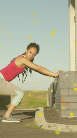 Multiple-yellow-spots-floating-against-african-american-fit-woman-performing-stretching-exercise