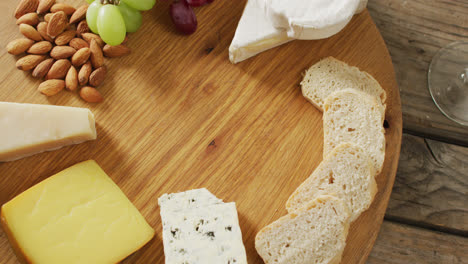 Video-Von-Käse,-Brot,-Nüssen-Und-Trauben-An-Bord,-Mit-Weinglas-Auf-Holztisch
