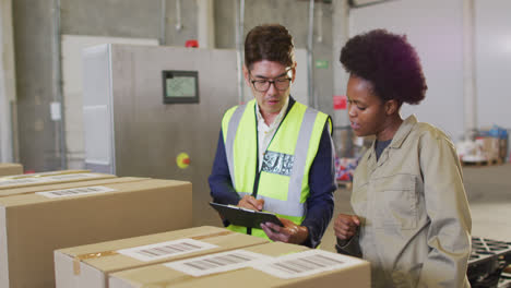 Diverse-male-and-female-workers-with-clipboard-and-boxes-in-warehouse