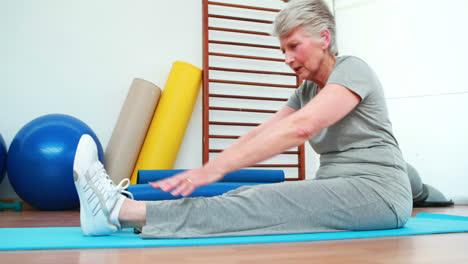 Elderly-woman-touching-her-toes-on-exercise-mat
