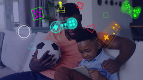 Animation-of-game-media-icons-over-smiling-father-and-son-using-tablet-on-couch-at-home