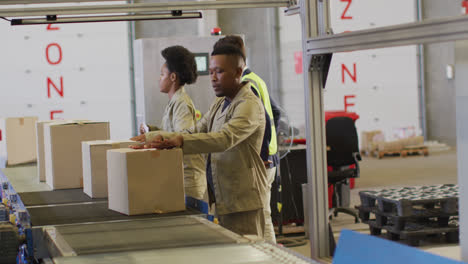 Diverse-male-and-female-workers-with-boxes-on-conveyor-belt-in-warehouse