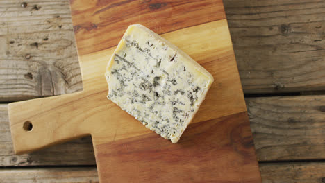 Video-overhead-shot-of-wedge-of-blue-cheese-on-chopping-board,-on-rustic-wooden-table