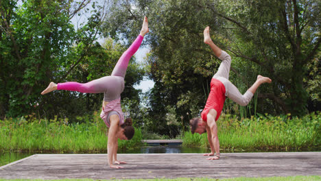 Kaukasische-Frau-Und-Mann-Praktizieren-Yoga-Im-Freien,-Stehen-Auf-Händen-Auf-Holzsteg-In-Der-Nähe-Von-Wald